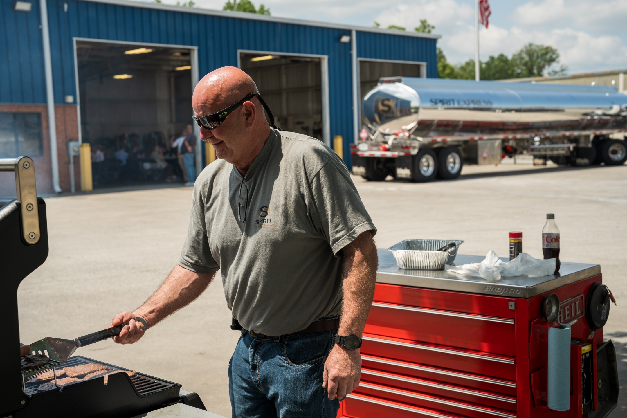 Man in sunglasses cooking on grill in front of tanker truck outside building