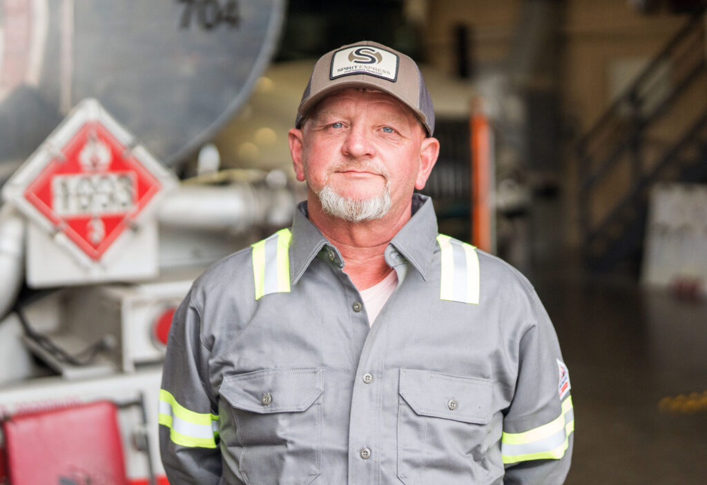 Truck Driver standing in front of truck in gray shirt.