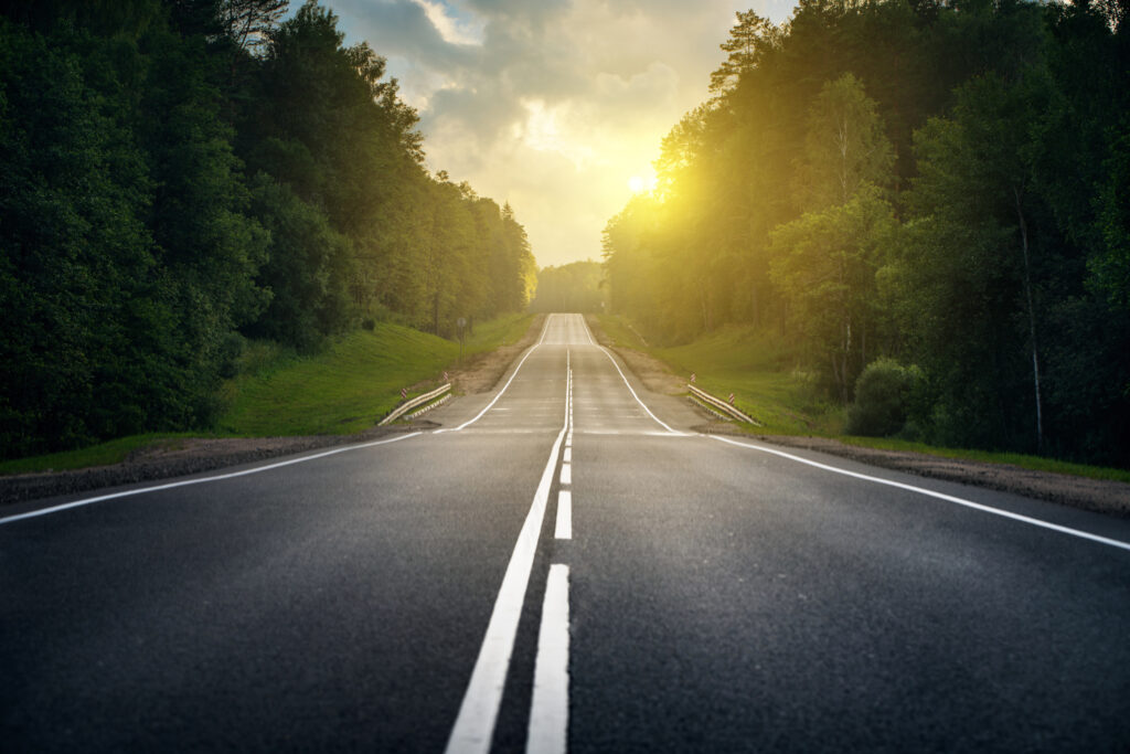 Photo of empty 2 lane highway at sunset with trees on both sides of road